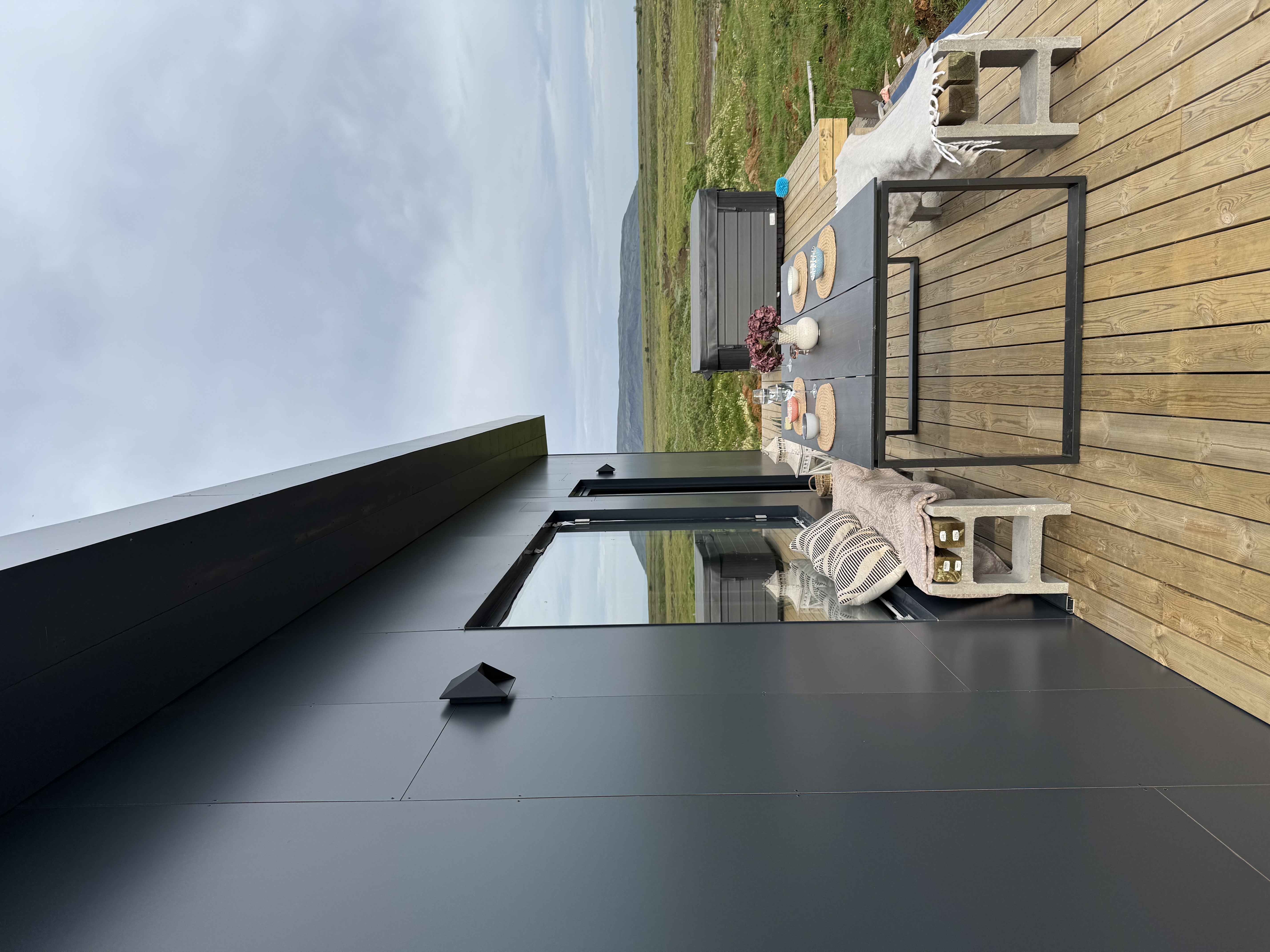 Outdoor dining table on a guesthouse terrace overlooking green Icelandic countryside and low hills.
